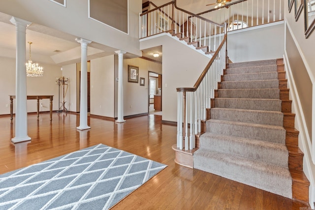 foyer featuring decorative columns, hardwood / wood-style flooring, a towering ceiling, and a notable chandelier