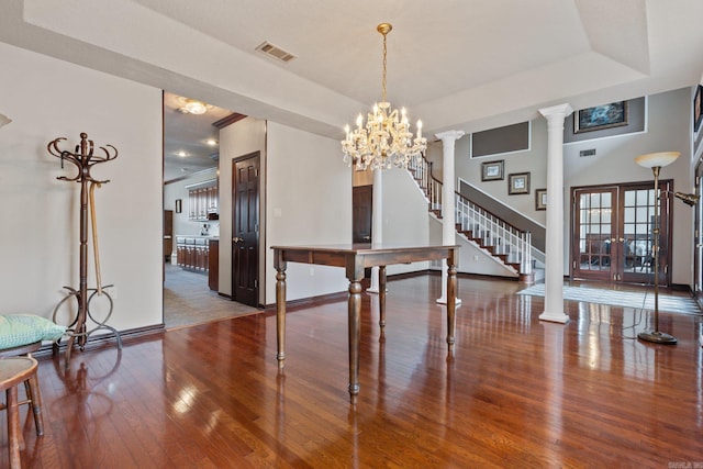 dining area with hardwood / wood-style flooring, a raised ceiling, decorative columns, and a notable chandelier