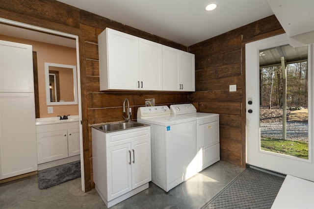 clothes washing area featuring washer and clothes dryer, wood walls, cabinets, and sink