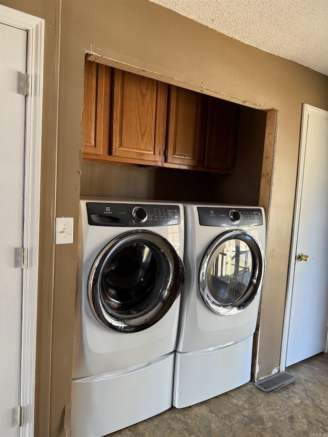 clothes washing area featuring washer and clothes dryer, cabinets, and a textured ceiling