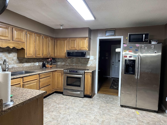 kitchen featuring backsplash, sink, stainless steel appliances, and a textured ceiling