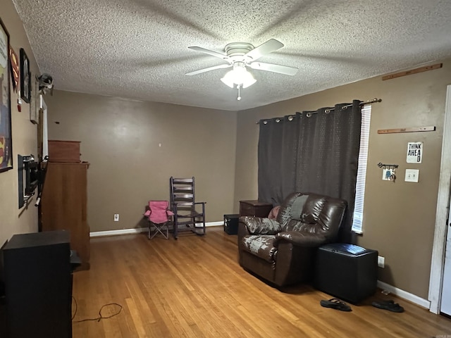 living area featuring hardwood / wood-style floors, ceiling fan, and a textured ceiling