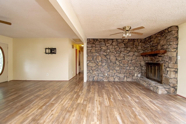 unfurnished living room featuring hardwood / wood-style floors, ceiling fan, a stone fireplace, and a textured ceiling