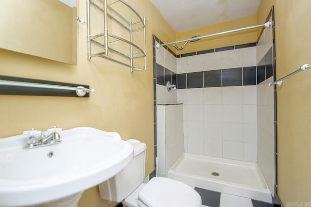 bathroom featuring a tile shower, toilet, and sink