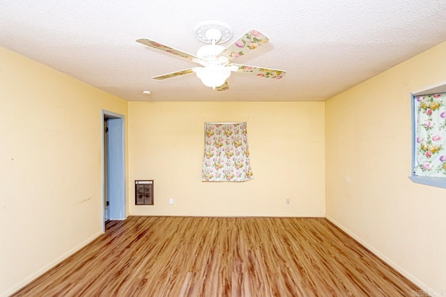 empty room featuring heating unit, ceiling fan, a textured ceiling, and light wood-type flooring