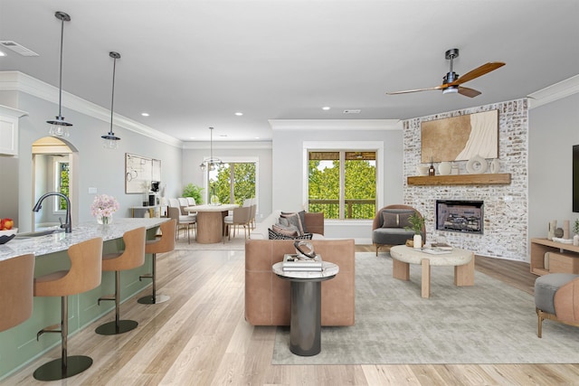 living room featuring a stone fireplace, ceiling fan, crown molding, and sink