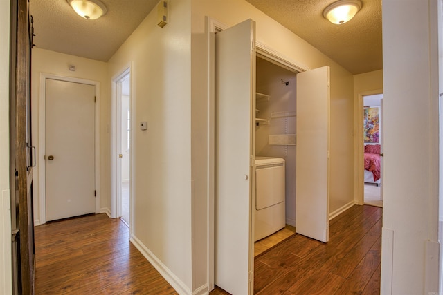 corridor with dark wood-type flooring, a textured ceiling, and washer / dryer