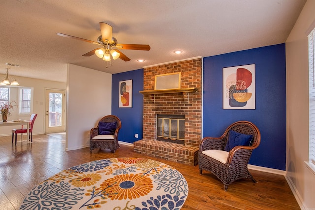 living room with hardwood / wood-style flooring, ceiling fan with notable chandelier, a textured ceiling, and a brick fireplace