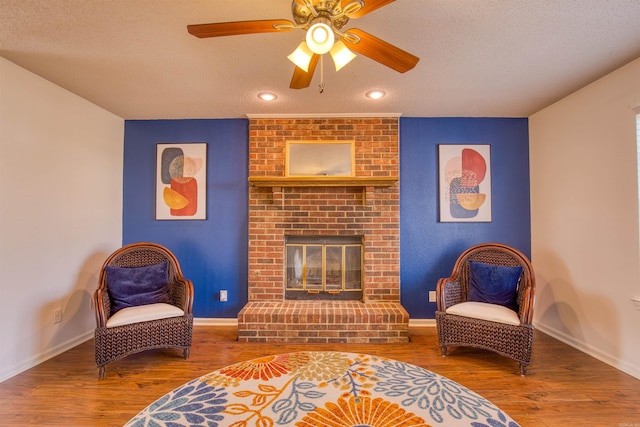 sitting room with hardwood / wood-style floors, a textured ceiling, a brick fireplace, and ceiling fan