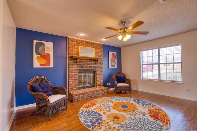 sitting room with a textured ceiling, hardwood / wood-style flooring, a brick fireplace, and ceiling fan