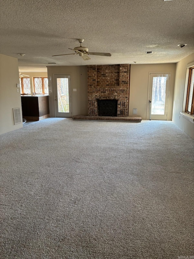 unfurnished living room with ceiling fan, carpet floors, a wealth of natural light, and a brick fireplace