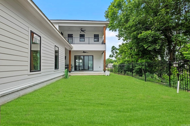 rear view of property with a balcony, ceiling fan, and a lawn