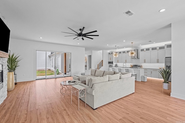 living room with light wood-type flooring, a stone fireplace, ceiling fan, and sink