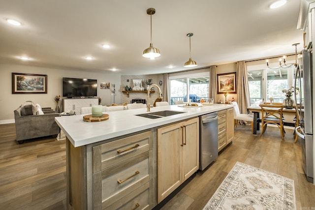 kitchen with sink, light brown cabinets, dark wood-type flooring, decorative light fixtures, and a center island with sink