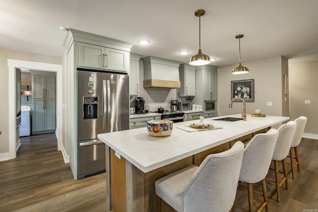 kitchen featuring sink, stainless steel appliances, premium range hood, washer / clothes dryer, and an island with sink