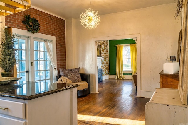 interior space featuring dark wood-type flooring, an inviting chandelier, brick wall, crown molding, and plenty of natural light