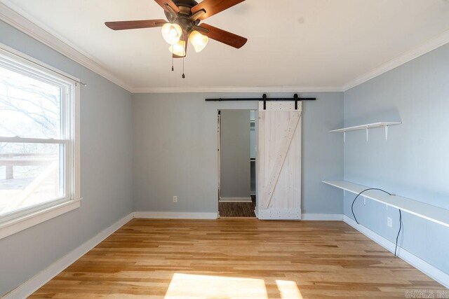 unfurnished room with baseboards, ceiling fan, ornamental molding, a barn door, and light wood-type flooring