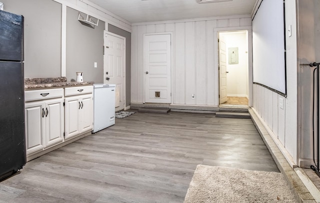 kitchen with black fridge, light hardwood / wood-style flooring, wood walls, fridge, and white cabinets