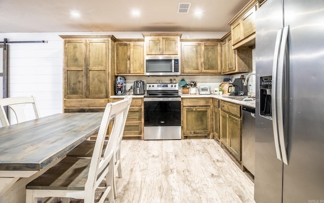 kitchen with a barn door, stainless steel appliances, light hardwood / wood-style flooring, and sink