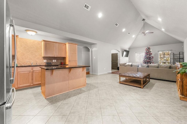 kitchen with ceiling fan, tasteful backsplash, stainless steel fridge, a breakfast bar, and a kitchen island