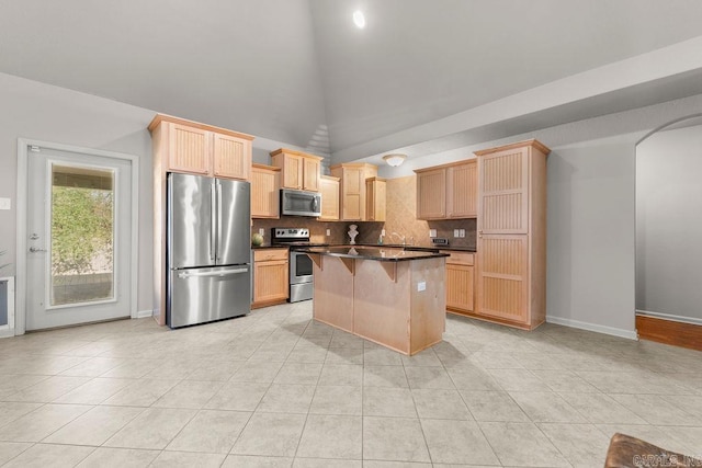 kitchen featuring appliances with stainless steel finishes, a breakfast bar, vaulted ceiling, light brown cabinets, and a kitchen island