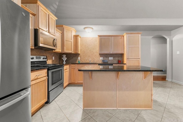 kitchen with a center island, stainless steel appliances, dark stone counters, a breakfast bar area, and light tile patterned floors