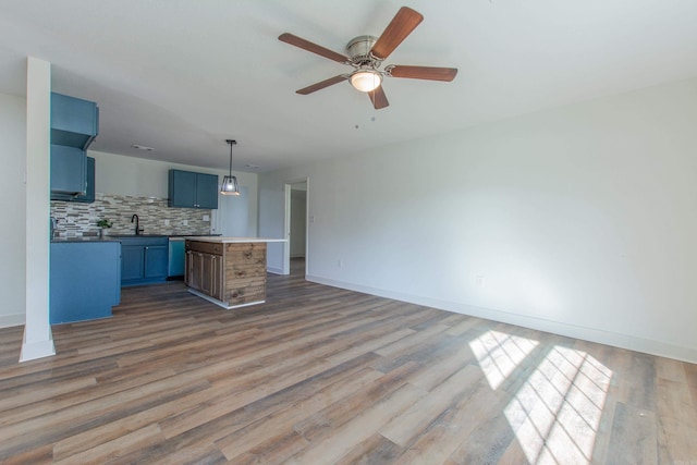 kitchen featuring blue cabinets, sink, hanging light fixtures, hardwood / wood-style flooring, and tasteful backsplash