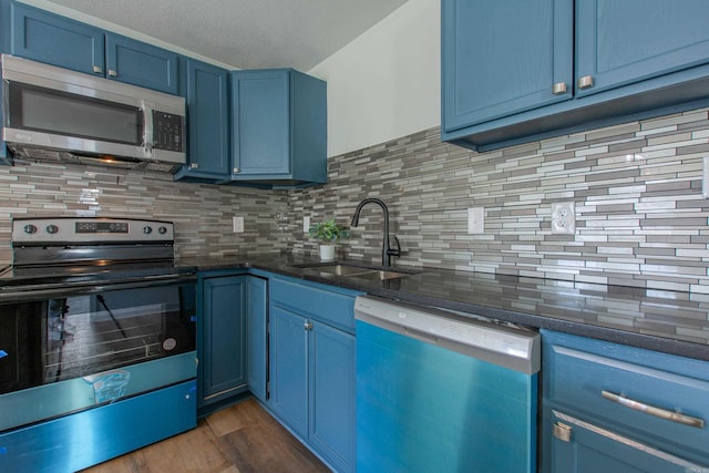 kitchen with blue cabinetry, sink, dark hardwood / wood-style flooring, decorative backsplash, and appliances with stainless steel finishes