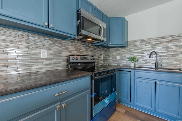 kitchen featuring decorative backsplash, appliances with stainless steel finishes, blue cabinets, dark wood-type flooring, and sink