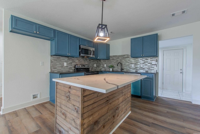 kitchen with blue cabinetry, appliances with stainless steel finishes, decorative backsplash, and light stone countertops