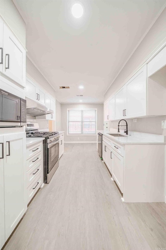 kitchen featuring white cabinets, sink, ornamental molding, appliances with stainless steel finishes, and light hardwood / wood-style floors