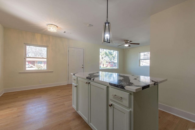 kitchen featuring ceiling fan, light stone countertops, light wood-type flooring, decorative light fixtures, and a kitchen island