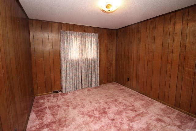 carpeted empty room with wooden walls and a textured ceiling