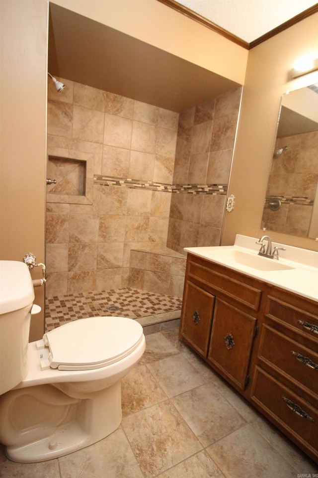 bathroom with vanity, toilet, ornamental molding, and a tile shower