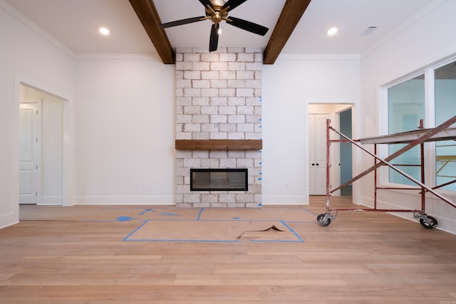 unfurnished living room with light wood-type flooring, ornamental molding, beamed ceiling, ceiling fan, and a fireplace