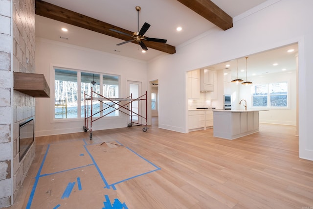 unfurnished living room featuring beam ceiling, a large fireplace, ceiling fan, and light hardwood / wood-style flooring