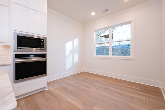 kitchen with white cabinetry, ornamental molding, light stone countertops, and appliances with stainless steel finishes