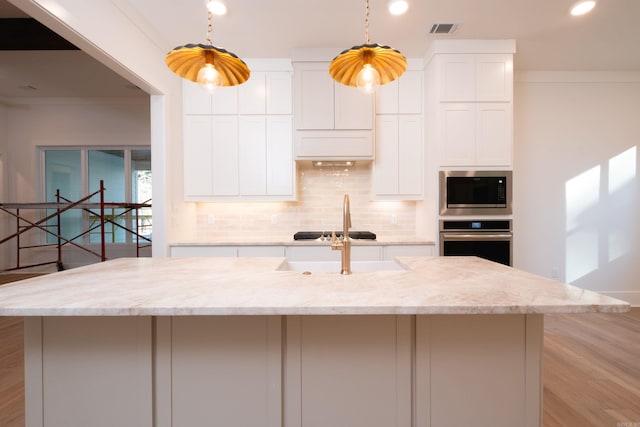 kitchen featuring crown molding, stainless steel appliances, light stone countertops, an island with sink, and white cabinets