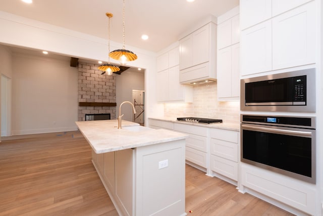 kitchen with decorative light fixtures, an island with sink, white cabinetry, sink, and stainless steel appliances