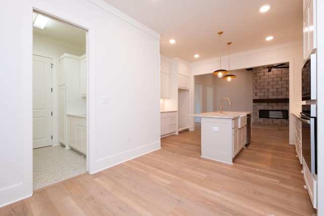 kitchen with pendant lighting, sink, a kitchen island with sink, white cabinetry, and ornamental molding