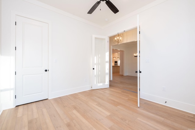 empty room with crown molding, ceiling fan with notable chandelier, and light wood-type flooring