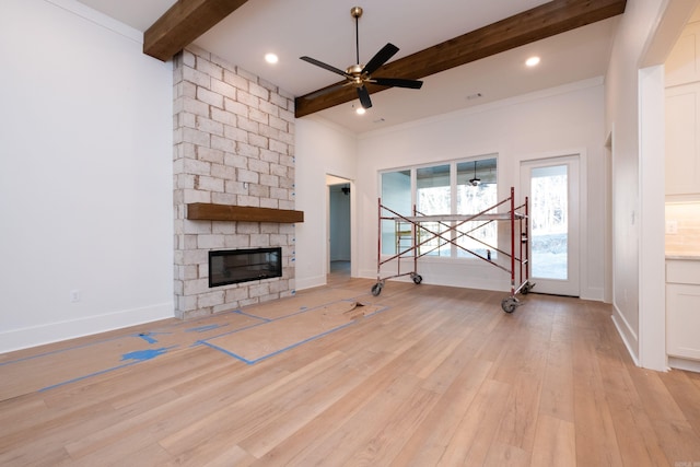 unfurnished living room with ceiling fan, beam ceiling, a fireplace, ornamental molding, and light wood-type flooring