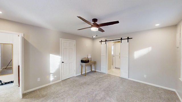 empty room with a barn door, light carpet, and ceiling fan