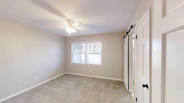 unfurnished bedroom with a barn door, ceiling fan, and light carpet