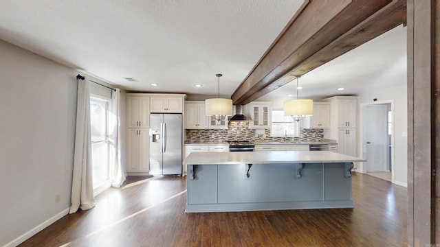 kitchen featuring a breakfast bar, wall chimney exhaust hood, appliances with stainless steel finishes, decorative light fixtures, and a kitchen island