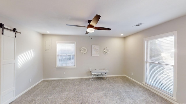 carpeted spare room featuring a barn door and ceiling fan