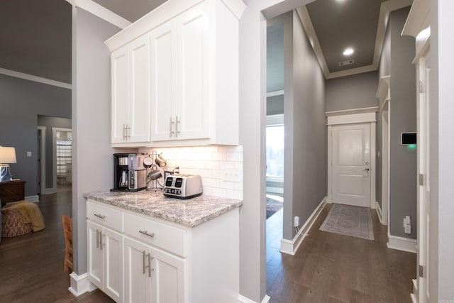 kitchen featuring light stone countertops, tasteful backsplash, crown molding, dark hardwood / wood-style floors, and white cabinetry