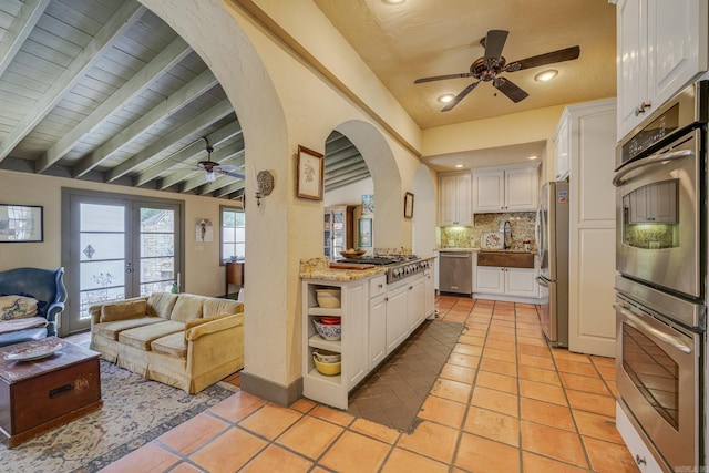 kitchen with backsplash, white cabinets, light tile patterned floors, beamed ceiling, and stainless steel appliances