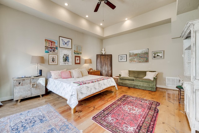 bedroom featuring ceiling fan, light hardwood / wood-style floors, and a high ceiling