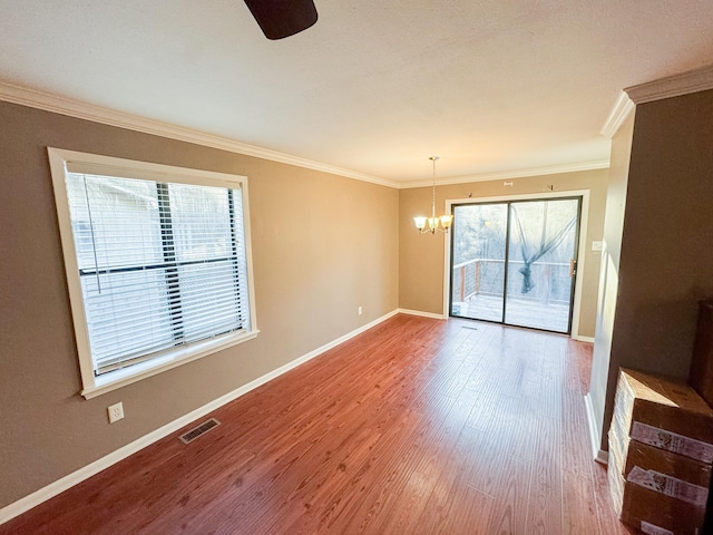 empty room with crown molding, an inviting chandelier, and hardwood / wood-style floors